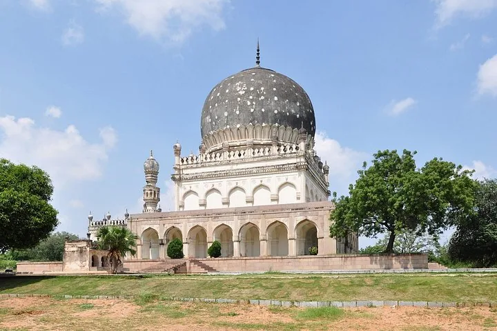 A large tomb with a black dome surrounded by trees and grass